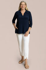 Woman wearing a navy top and white pants on a beige background